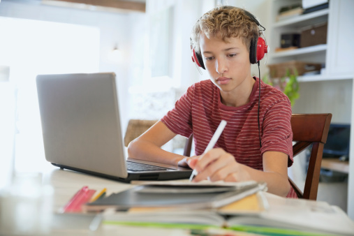 young-boy-writing-notes-with-red-headphones-on-studying-online